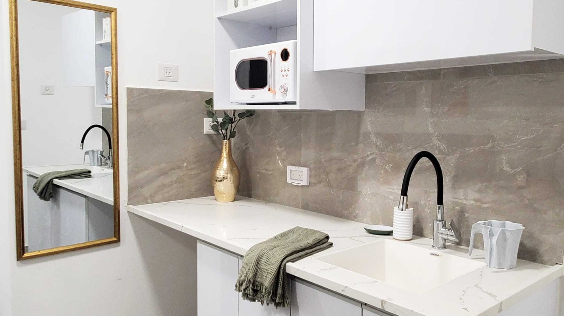 The kitchenette: white marble-look counter, black faucet, gold vase and a gold-framed mirror